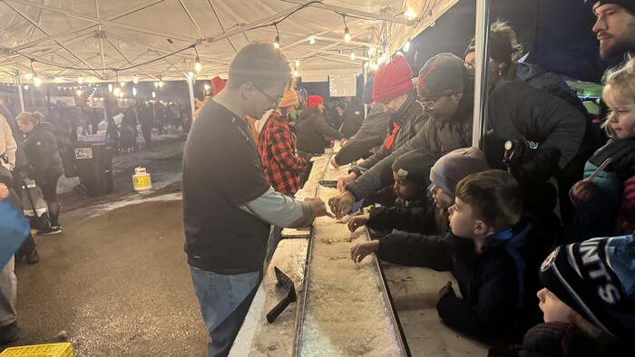 Des enfants s'essaient à la tire d'érable, en déposant un bâtonnet sur du sirop d'érable versé sur de la glace.
