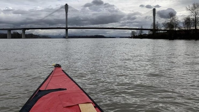 La pointe d'un canot sur l'eau devant un pont. 