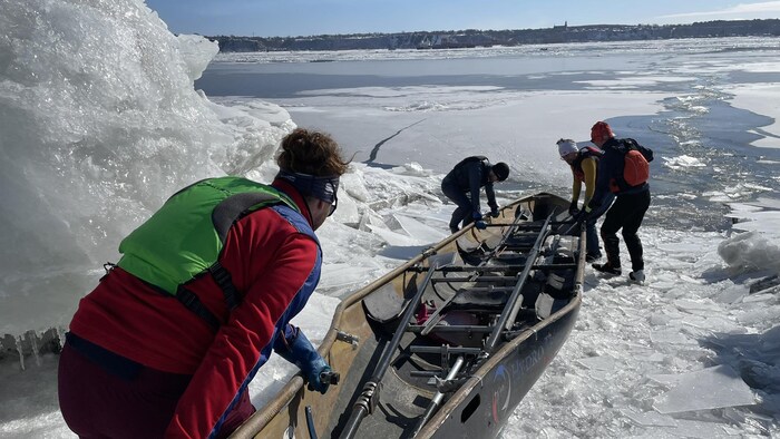 Quatre membres de l'équipe poussent et tirent un long canot sur la glace pour le mettre à l'eau.