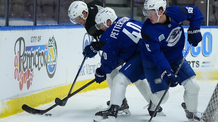 Trois joueurs de hockey essaient de récupérer une rondelle à l'aide de leur bâton.