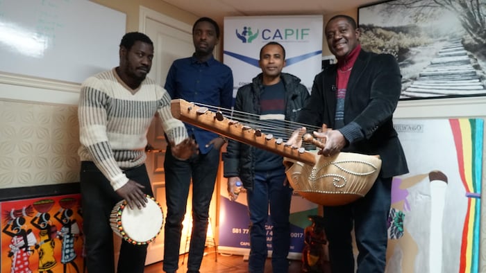 Le président du CAPIF, Claude Hervé Kouassi, à droite, accompagné de travailleurs immigrants. Deux ont des instruments de musique à la main.