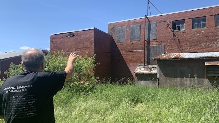 Un homme debout, derrière une usine abandonnée.