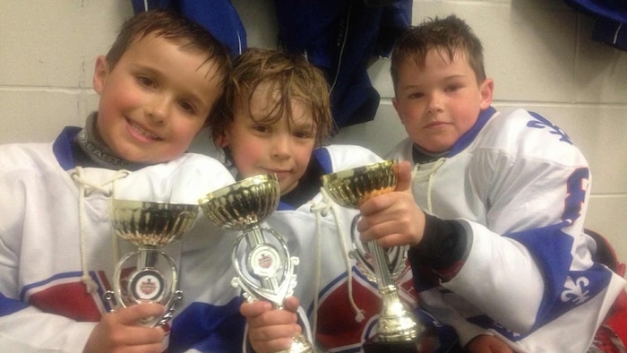 Les trois garçons tiennent un trophée.