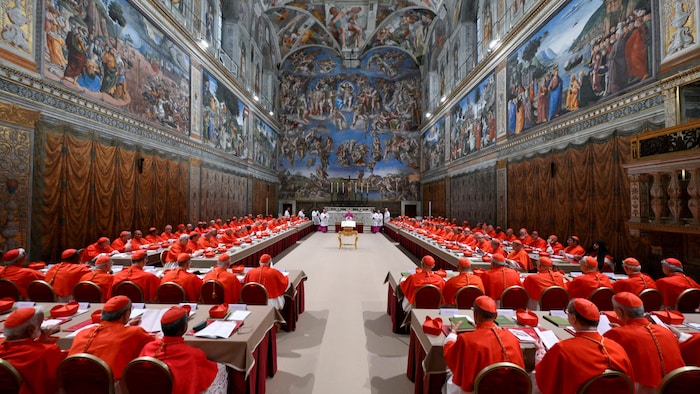 Une foule de cardinaux prient dans une chapelle peinte de grandes fresques.
