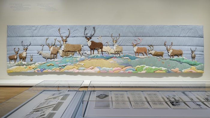 Une grande toile en courte pointe montre plusieurs caribous sur une terre désertée.