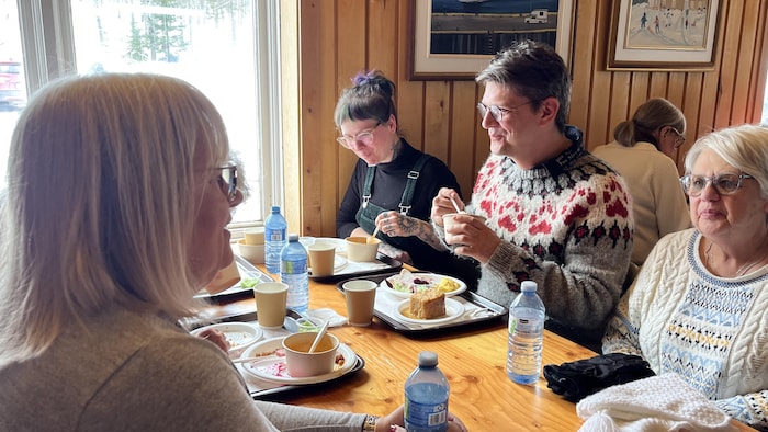 Carl Desrosiers attablé avec d'autres personnes, souriant à sa voisine.