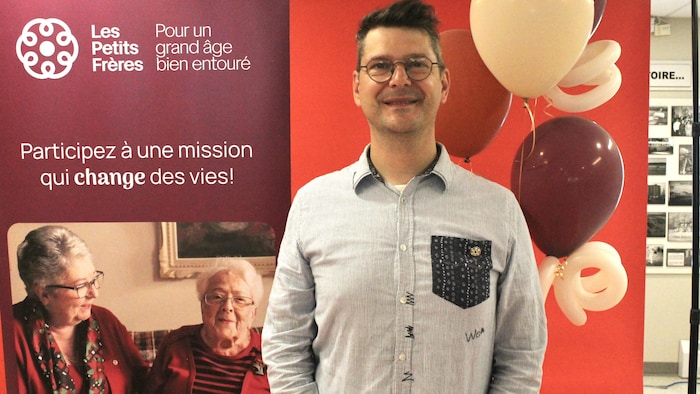 Carl Desrosiers pose devant les ballons et l'affiche promotionnelle.