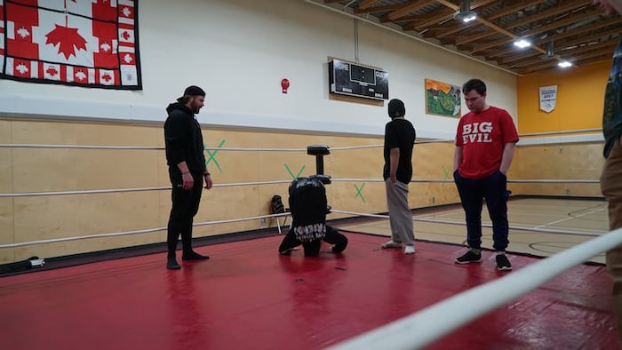 Des lutteurs dans un gymnase observent un jeune en train de faire une roulade.