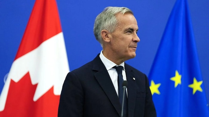 Mark Carney devant des drapeaux du Canada et de l'Union européenne.
