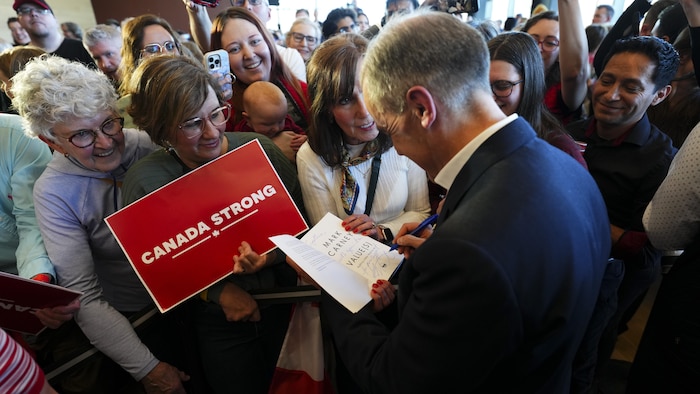 Mark Carney autographie un livre.