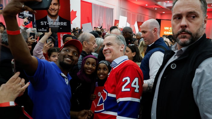 Une personne prend une photograph avec Mark Carney dans un rassemblement.