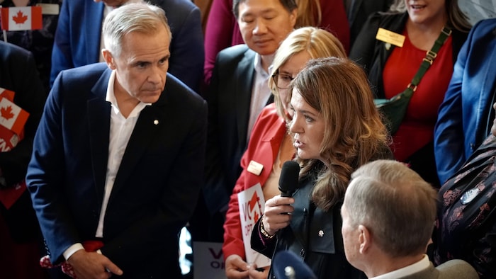 Mark Carney regarde avec attention Danielle Smith, qui parle à un micro dans une brasserie de Red Deer.