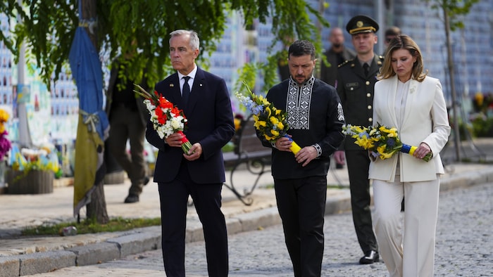 Mark Carney, Volodymyr Zelensky et Olena Zelenska marchent en tenant des gerbes de fleurs.