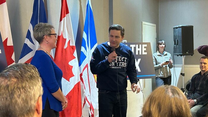 Pierre Poilievre parle dans un micro qu'il tient dans sa main. Carol Anstey est à sa droite, de profil.