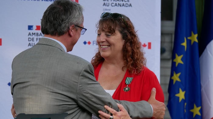 A carol doucet becomes signet light smiling woman and a back man in front of banners of France.