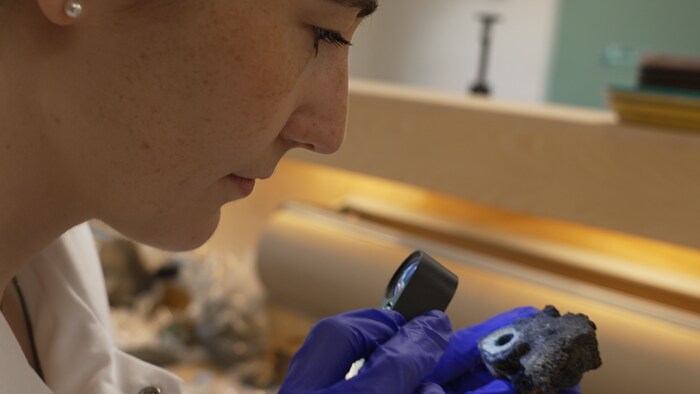 Une femme examine une rocher avec une loupe.