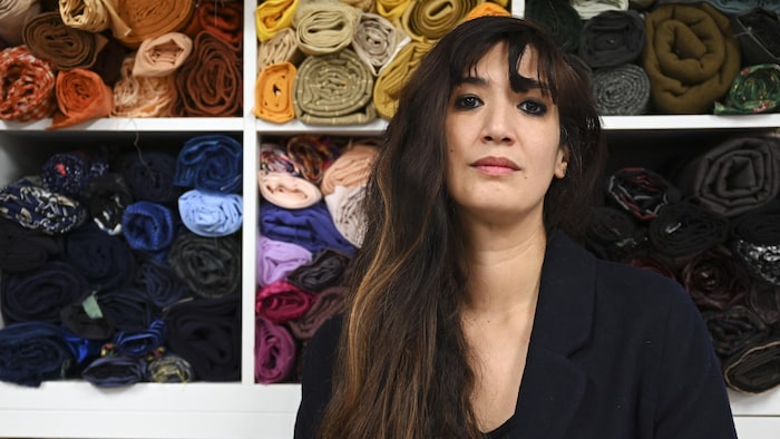 Une femme aux longs cheveux bruns airs devant des tissus.