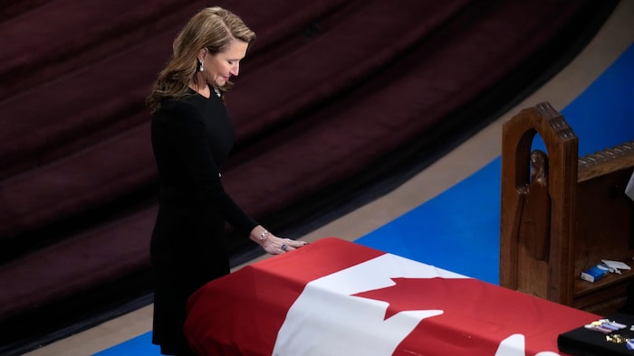 Caroline Mulroney touche le cercueil de son père, qui est recouvert d'un drapeau du Canada.
