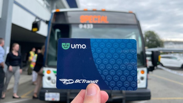 Une personne tient une carte Umo de BCTransit devant un bus.