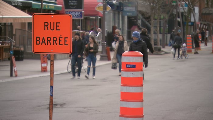 Un panneau orange indique que la rue est barrée. En arrière-plan, des gens déambulent sur l'avenue Cartier, à Québec.