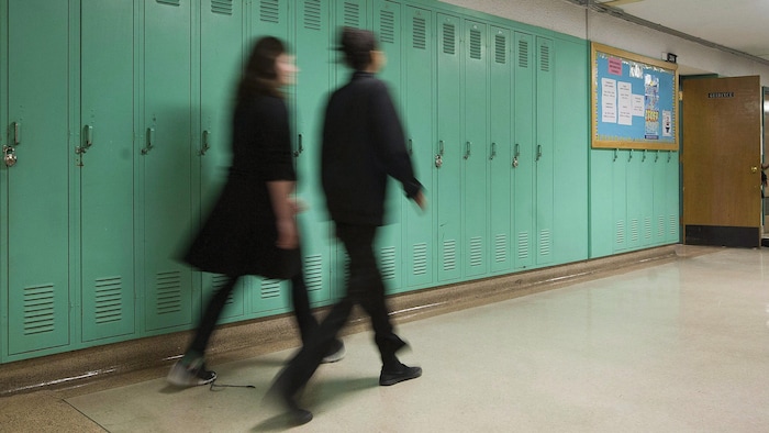 Des élèves marchent devant des casiers dans un corridor d'école.