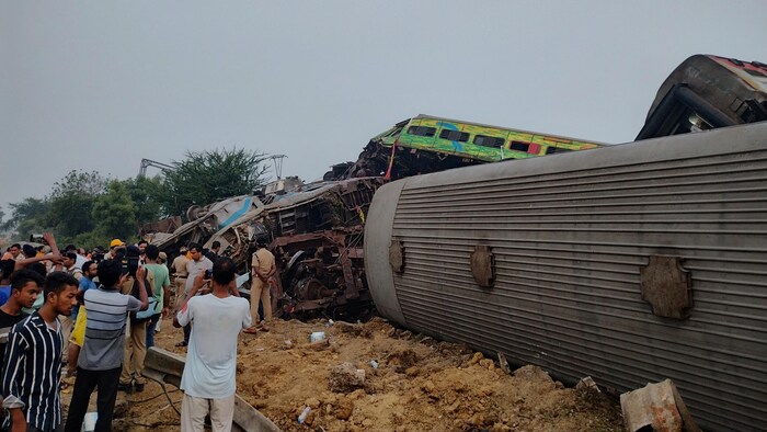 Des secouristes et des curieux se tiennent à côté de wagons endommagés, après la collision de trains à Balasore, en Inde, le 3 juin 2023, dans cette photo obtenue sur les médias sociaux. 