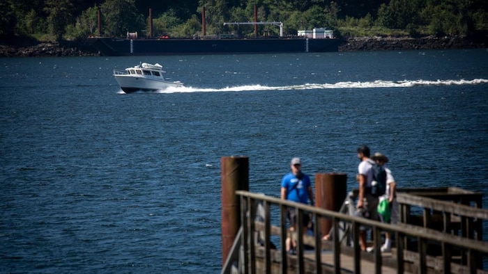 Une vue d'un ponton qui s'avance depuis Cates Park sur l'eau. Deux navires en second plan, une vedette et une péniche.