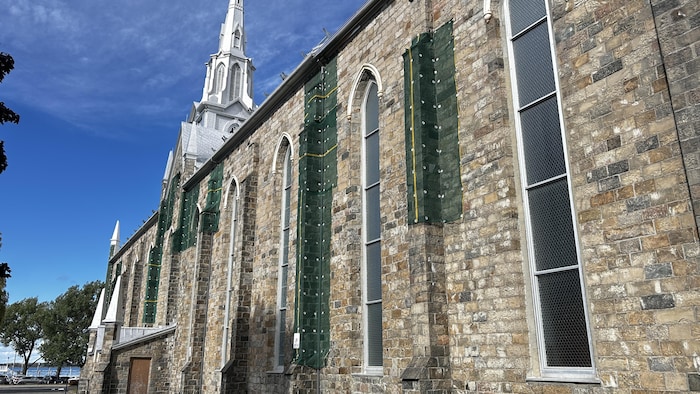 Un mur externe de la cathédrale de Rimouski présentant des membranes vertes qui doivent retenir la pierre.