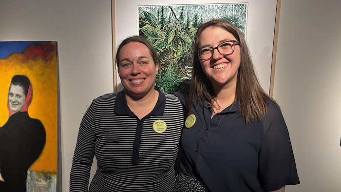 Plan moyen de deux femmes souriantes se tenant côte à côte dans une galerie d'art.