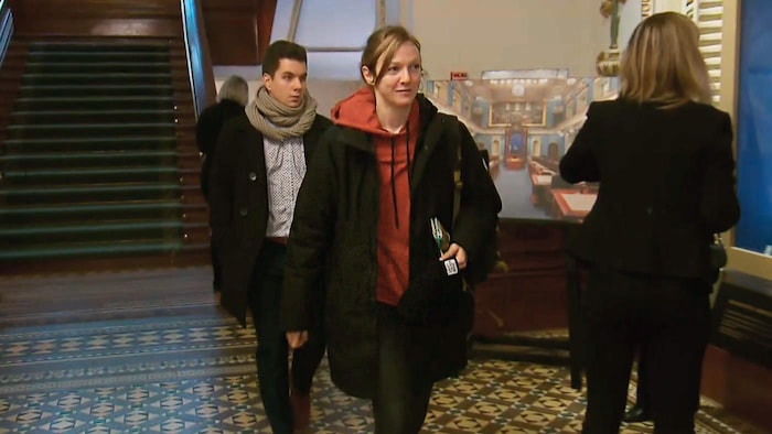 Catherine Dorion porte un coton ouaté orange qu'on aperçoit sous un manteau noir. 