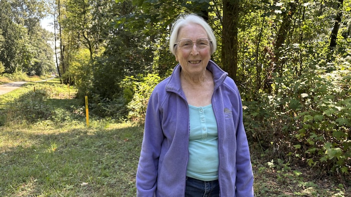 Une femme en chandail mauve devant un sentier en forêt.