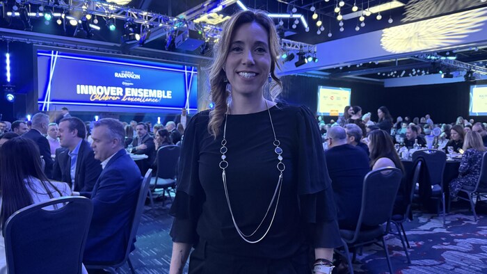Une femme debout dans une salle de gala sourit à la caméra.