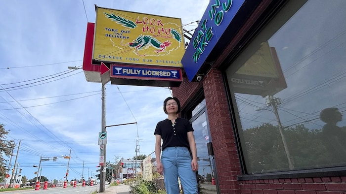 Photo en contreplongée d'une femme debout sur le trottoir sous une enseigne jaune décorée d'un dragon vert.