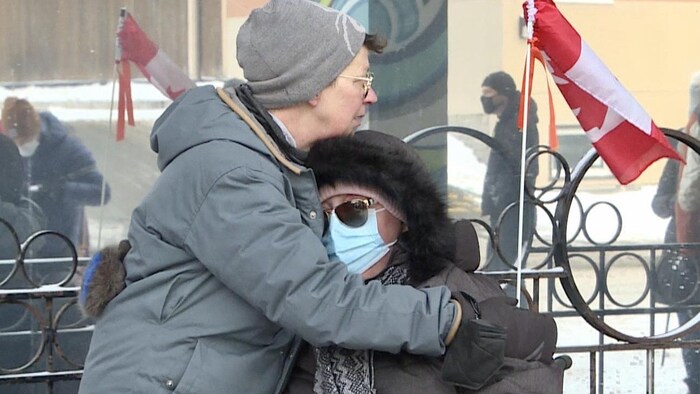 Une femme réconforte une autre femme masquée, à l'extérieur à Ottawa.