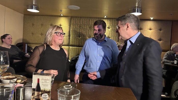 Une femme et deux hommes autour d'une table. 