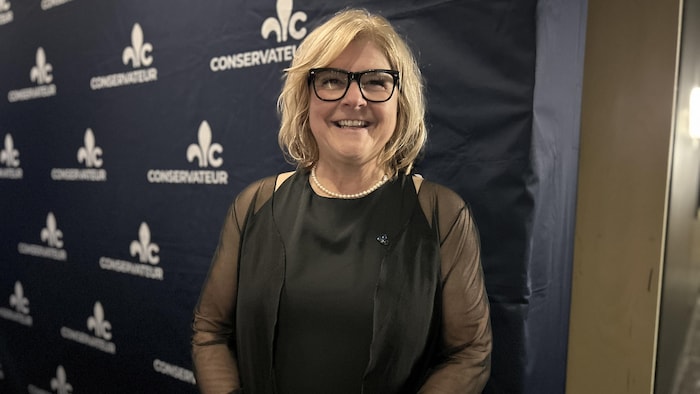 Catherine Morissette sourit devant une affiche du Parti conservateur du Québec.