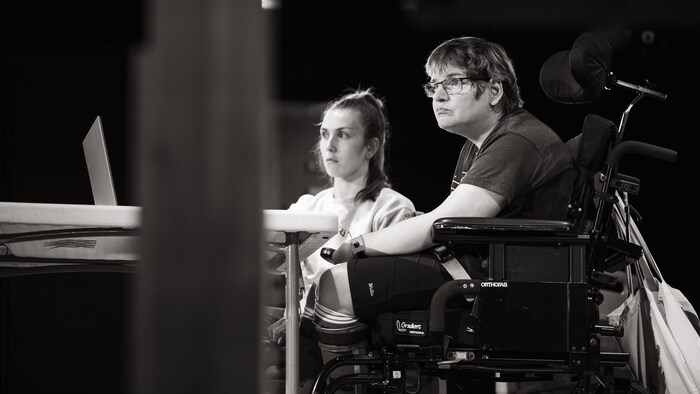 Deux personnes attentives devant un ordinateur, dont l'une est installée dans un fauteuil roulant.