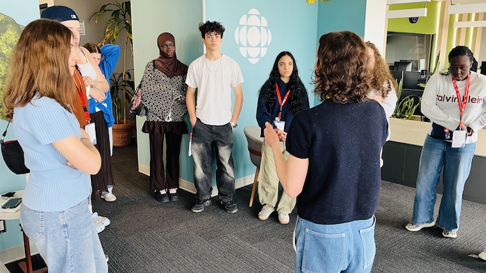 Une jeune femme parle à des jeunes qui forment un cercle autour d'elle, dans les locaux de Radio-Canada, à Sept-Îles.