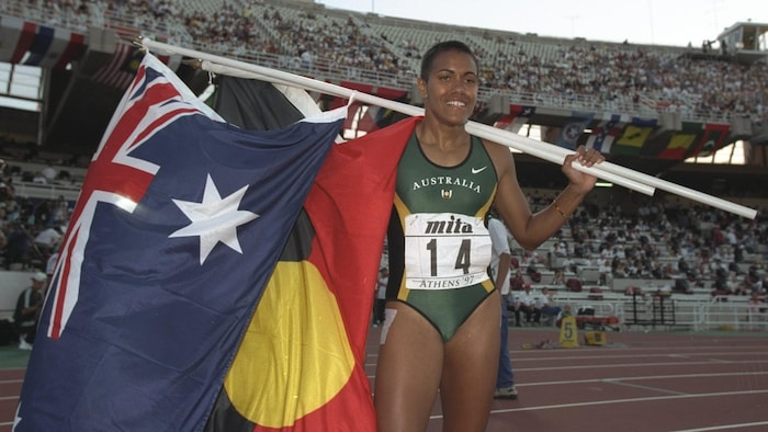 L'athlète pose pour les photographes avec le drapeau aborigène et le drapeau australien.