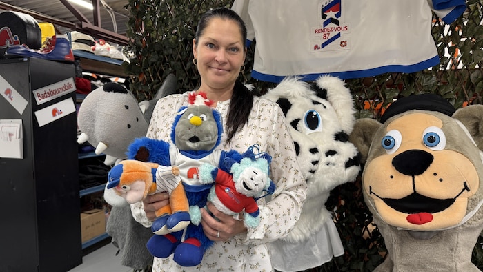 Une femme sourit pour la photo et tient des mascottes en peluche dans ses mains.