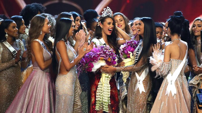 Hawak ni Catriona Gray ang kanyang korona at napapalibutan ng iba pang kandidata sa Miss Universe pageant.