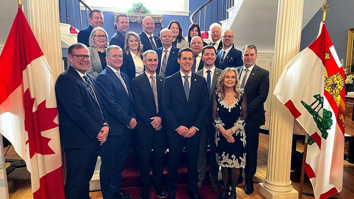 Dix-huit personnes debout sur trois rangées pour une photo de groupe en bas d'un escalier, avec un drapeau du Canada sur pied à gauche et un drapeau de l'Île-du-Prince-Édouard à droite.