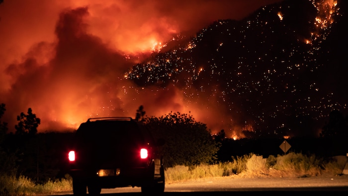 Un automobiliste arrêté au bord de la route Transcanadienne observe un feu de forêt à flanc de montagne à Lytton, en Colombie-Britannique, le jeudi 1er juillet 2021.