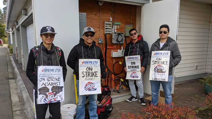 Quatre employés portant des pancartes de grève manifestent près d'un panneau de télécommunications à Port Coquitlam, en Colombie-Britannique. Photo non datée.