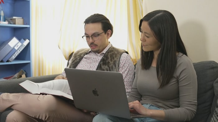 Un homme et une femme sont assis sur un canapé et consultent des documents sur un ordinateur portable et dans un livre de droit, à Iqaluit, au Nunavut, en juillet 2025.