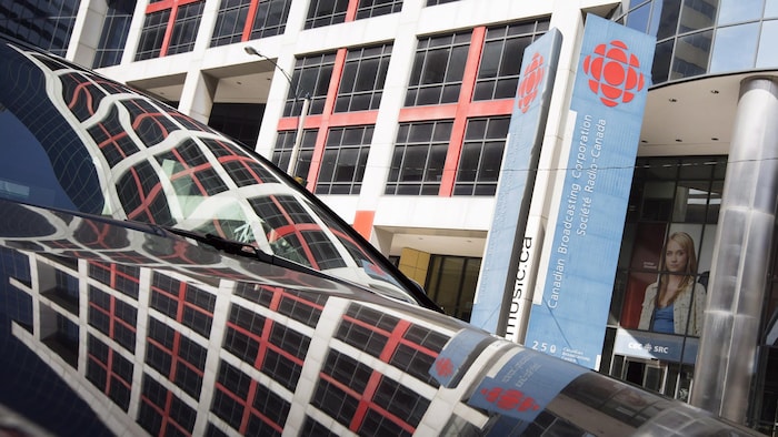 Les fenêtres de la maison de Radio-Canada à Toronto se reflètent dans une voiture stationnée devant l’édifice.