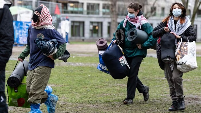 Sur un terrain, des personnes masquées portent des sacs.