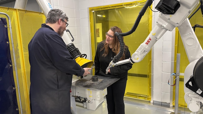 Un professeur et son étudiante observent le travail de soudure effectué par un robot articulé.