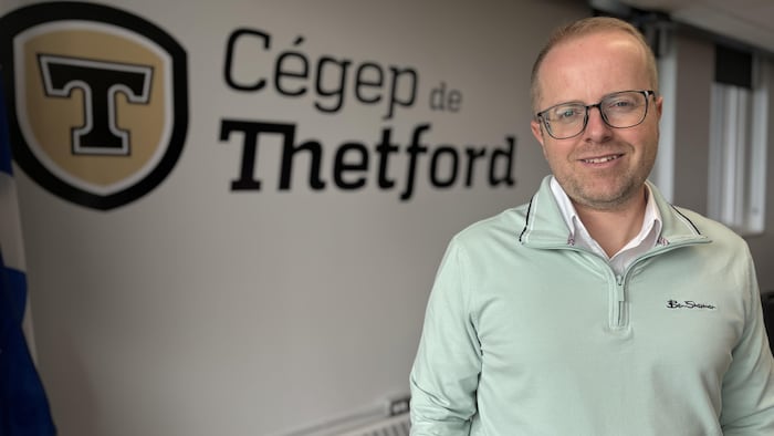 Un employé du Cégep de Thetford posant devant le logo du cégep.
