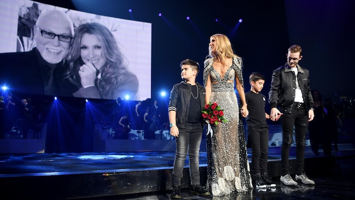 Un bouquet de fleurs à la main, Céline Dion regarde une photo d'elle et de René Angélil, aux côtés de ses trois enfants.